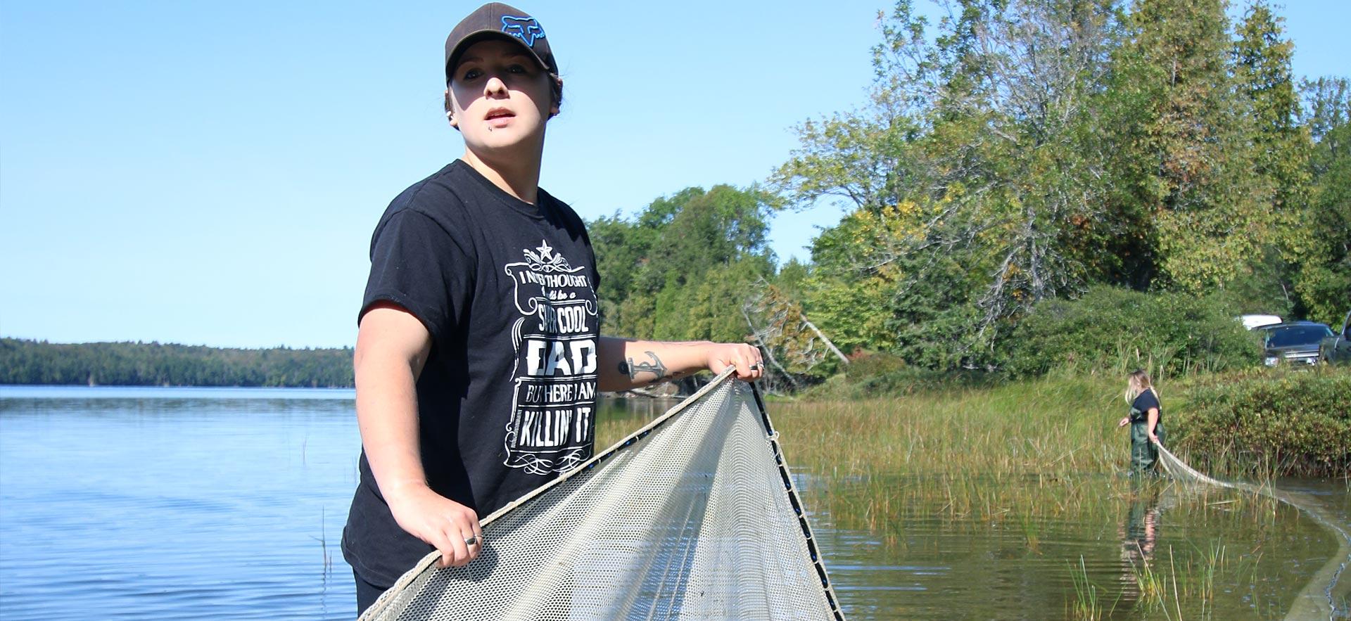 A female Fish and Wildlife Conservation Technician student sets a net in the water.