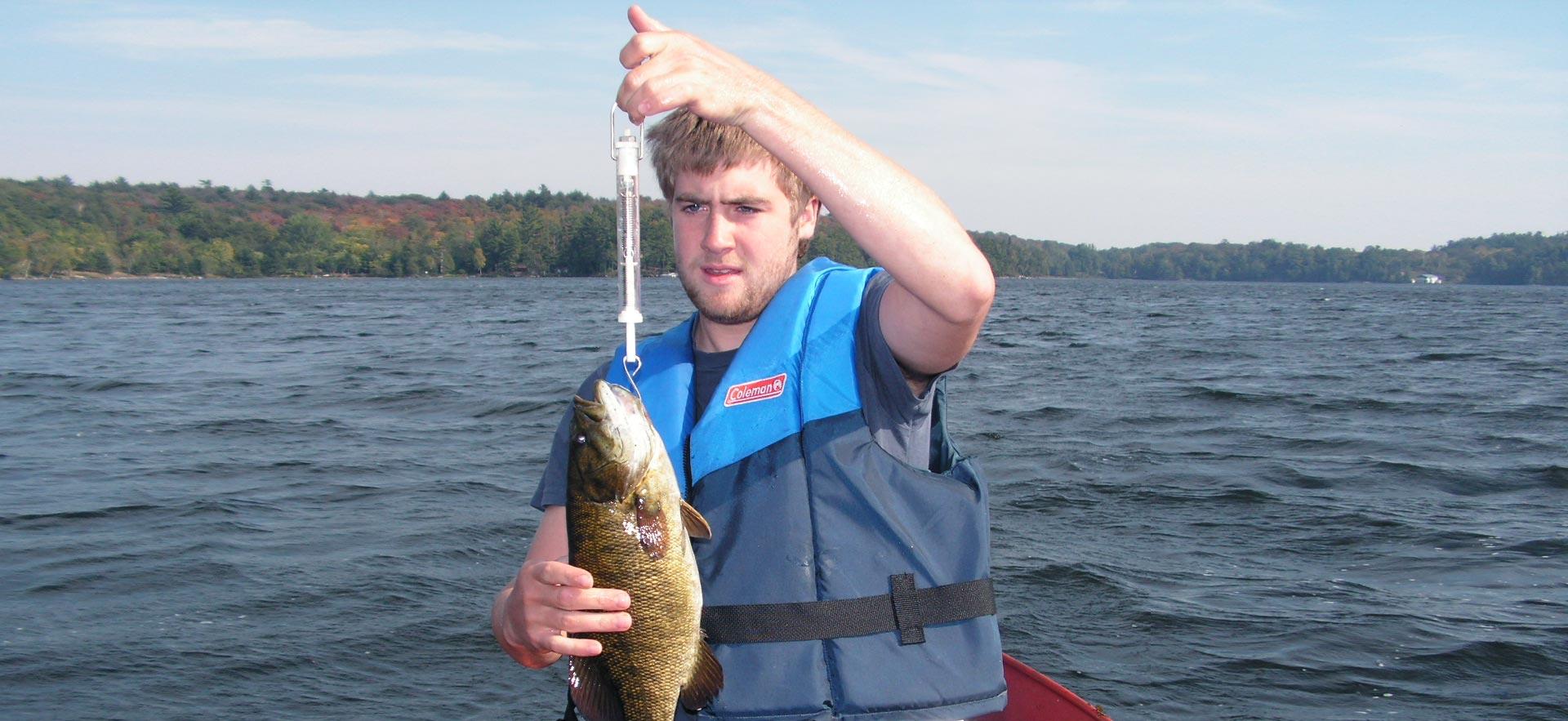 A male Fish and Wildlife student weighs a fish.