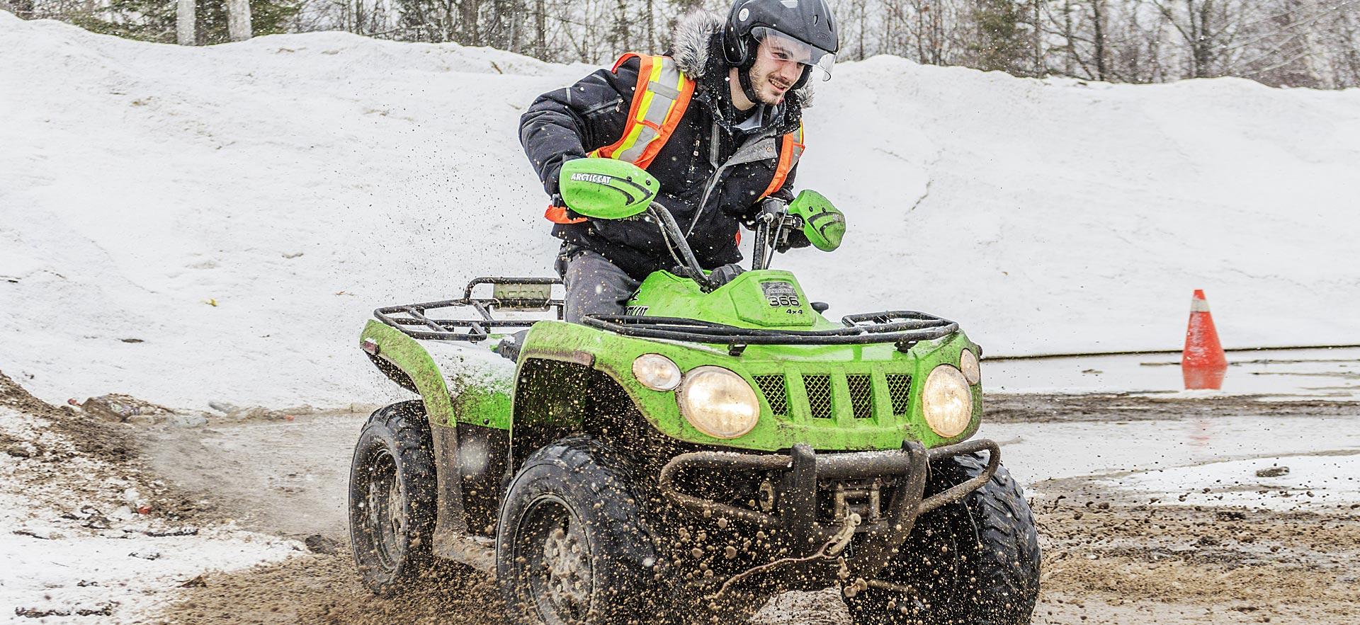 Male student rides an all terrain vehicle through snow and mud.