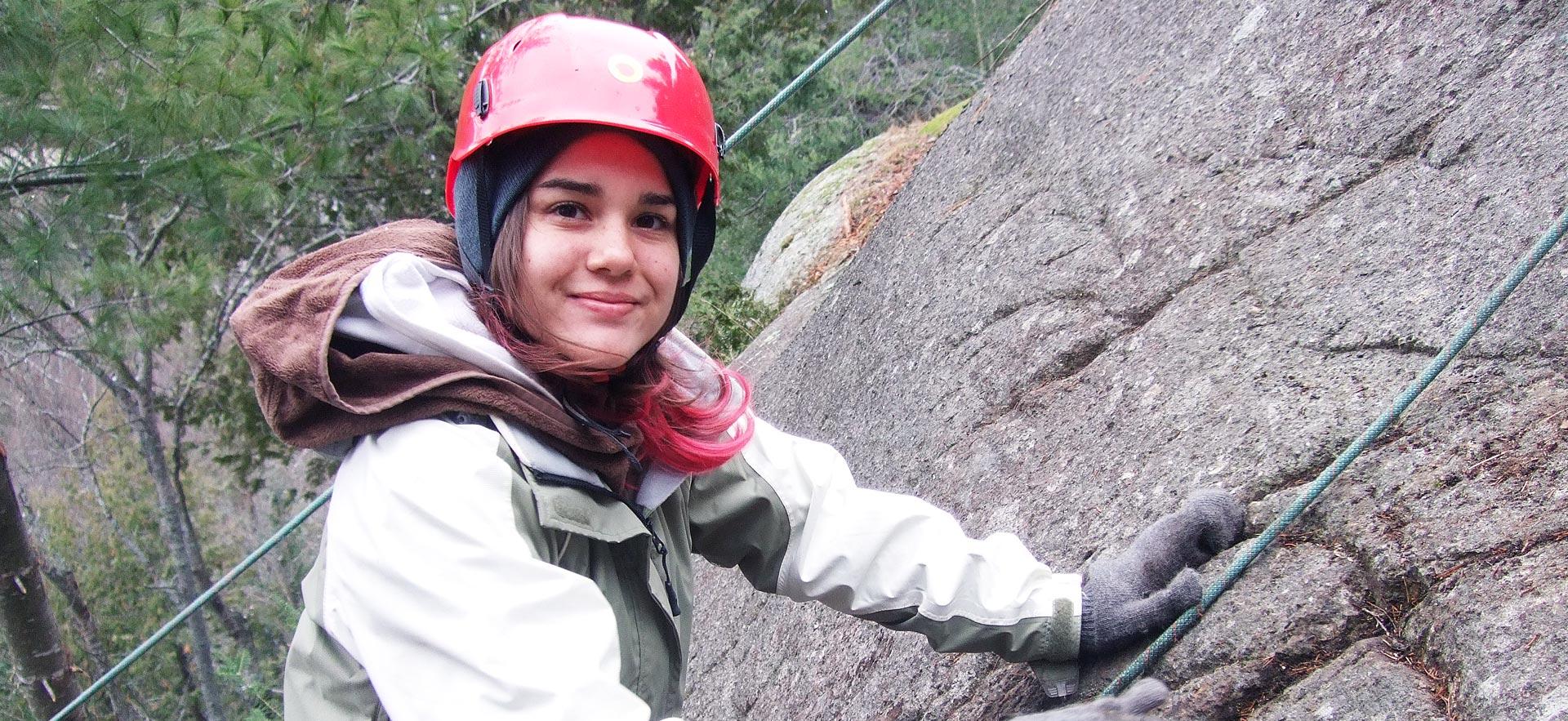 female student smiles for camera while rock climbing.