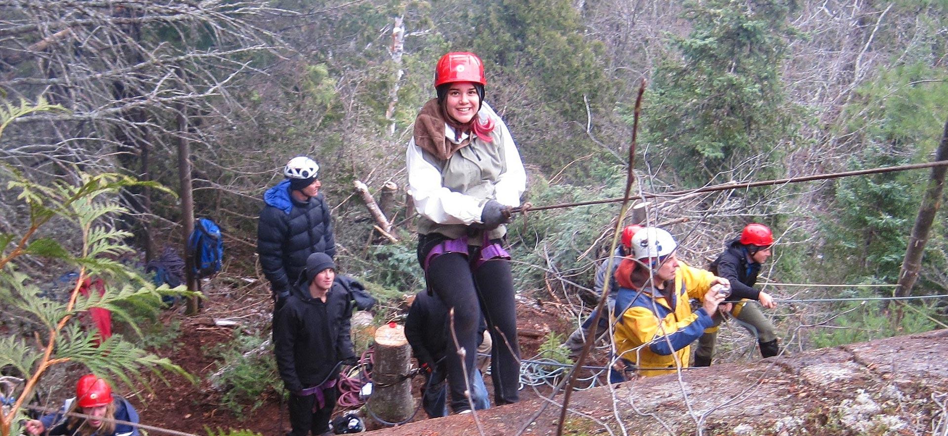 Female student smiles for camera while rock climbing.
