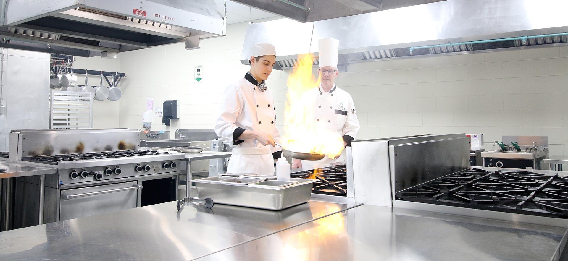 A male culinary student gets instruction on how to create a flambe in one the culinary kitchens.