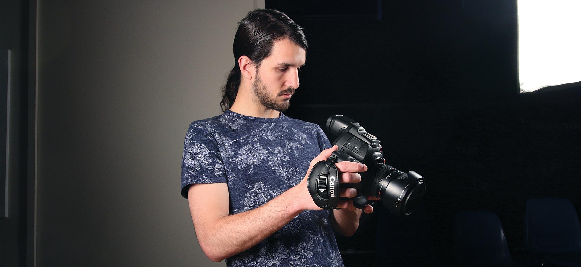 Male digital video student checks the setting on his camera.