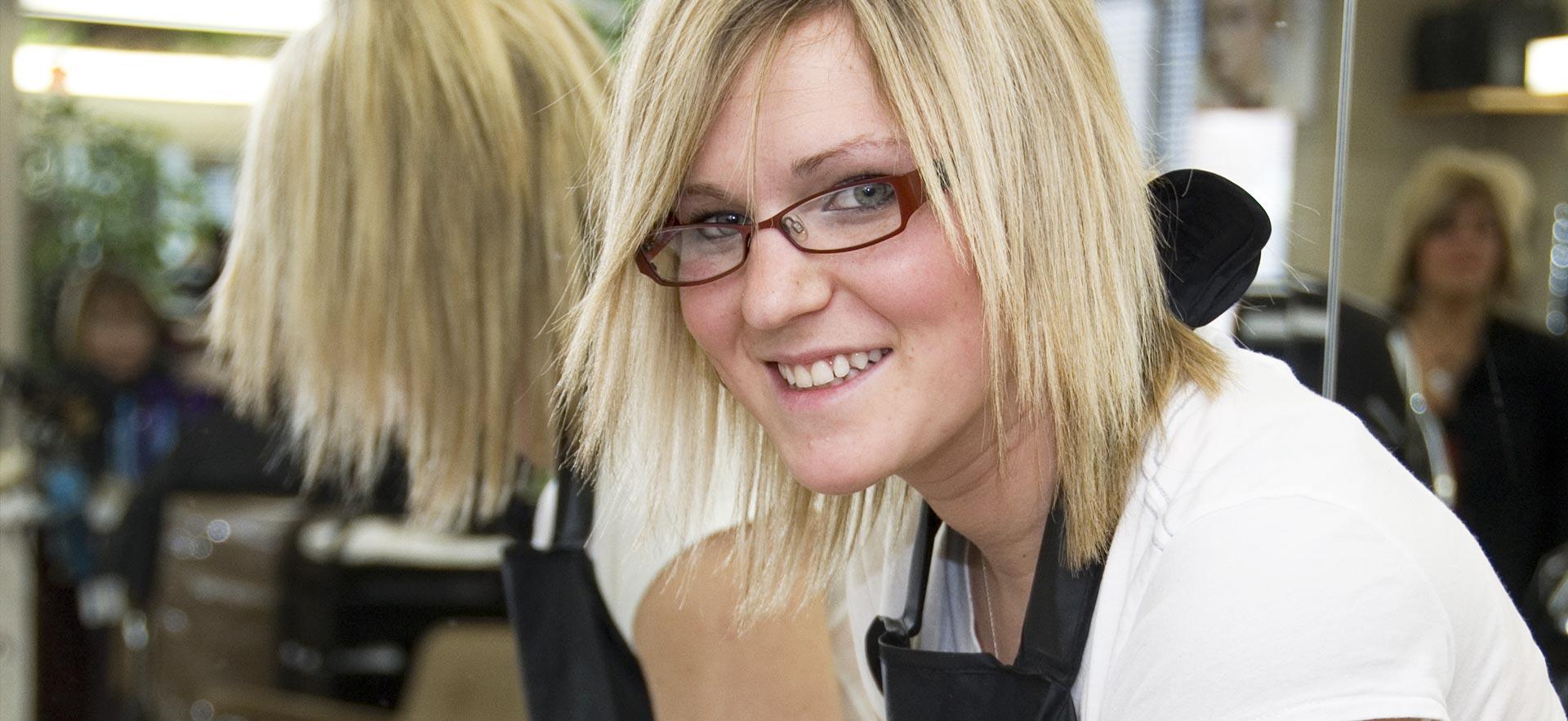 A female hairstylist student smiles for the camera in the hairstyling salon.