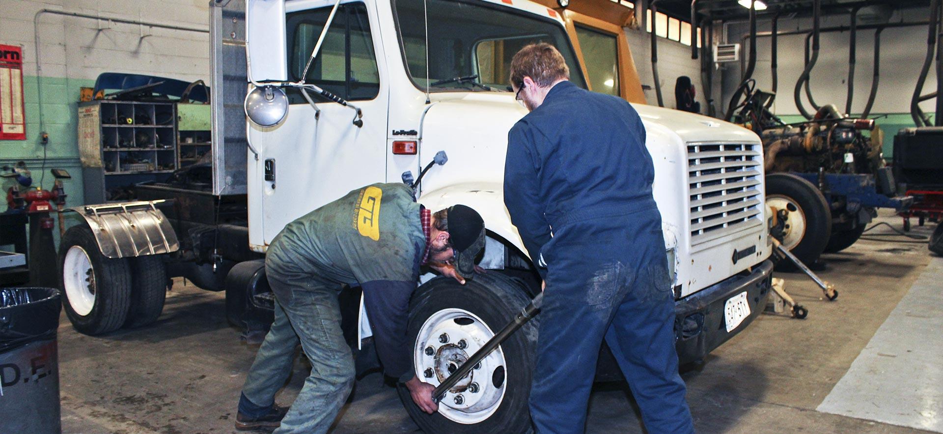 Two male heavy equipment students work on a truck.