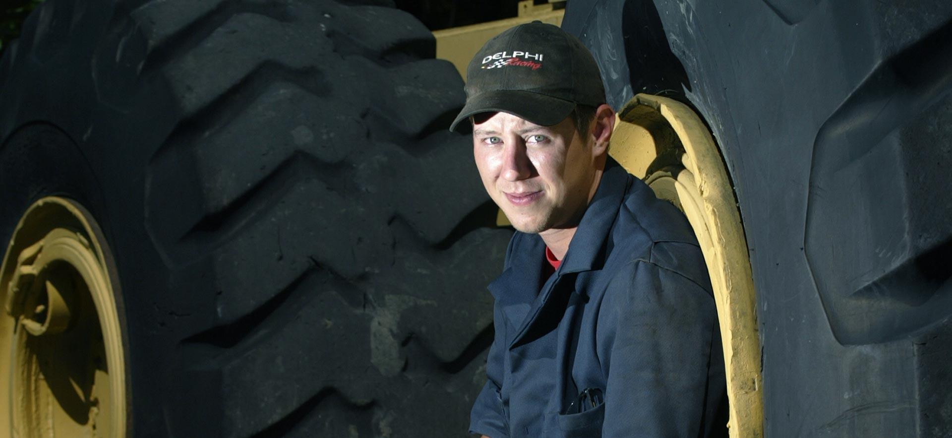 One male heavy equipment student poses for a photo in front of some truck tires..