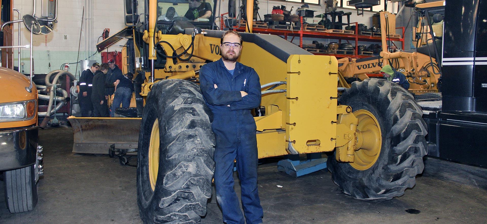 One male heavy equipment student poses for a photo in front of a tractor truck.
