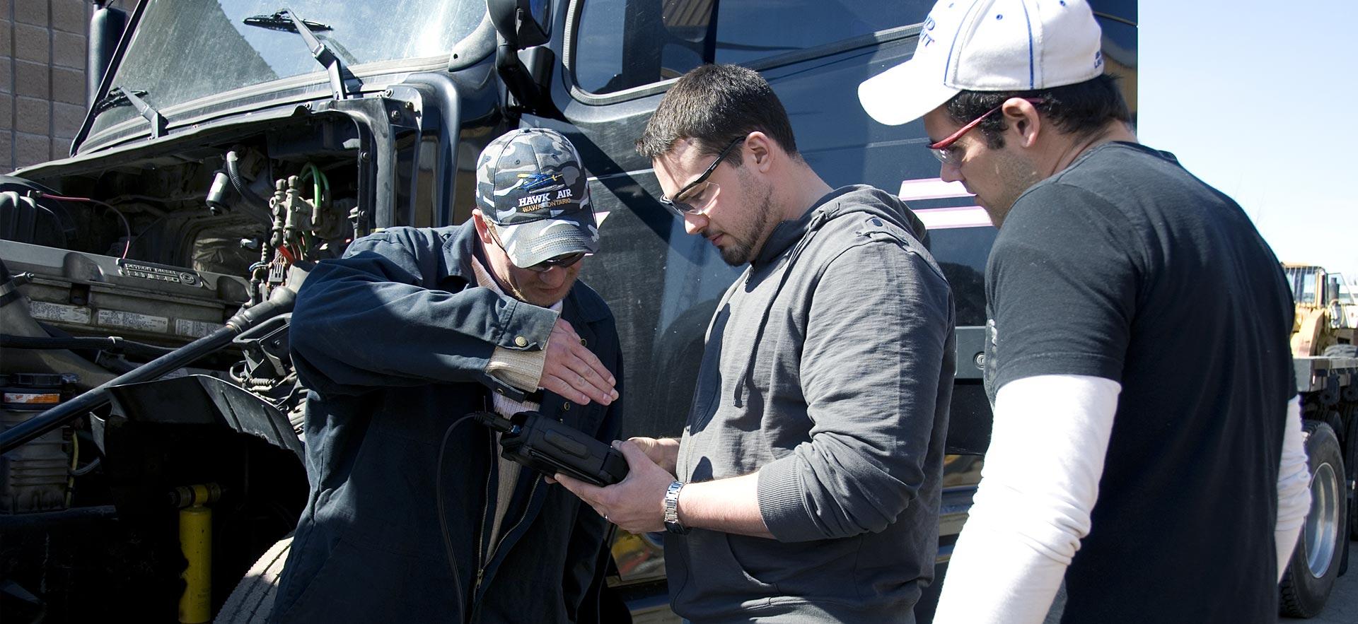 A group of male heavy equipment students discuss repairs on a truck.