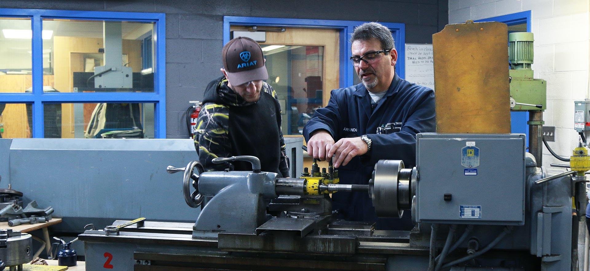 One male machine shop student working on a class project with the help of his instructor.