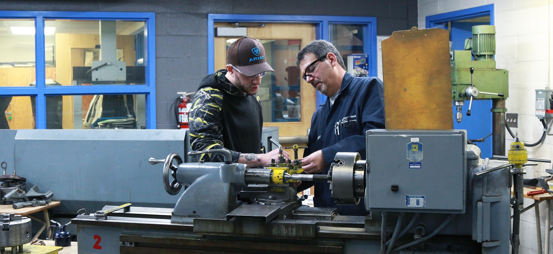 One male machine shop student working on a class project with the help of his instructor.