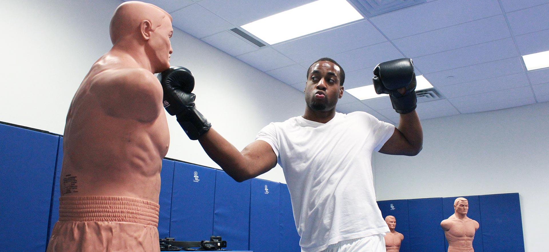 Male Police Foundations student practices on a Criminal Punching Boxing Dummy.