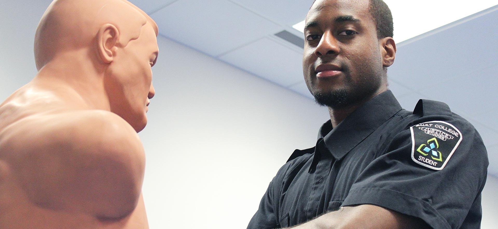 Male Police Foundations student poses next to a Criminal Punching Boxing Dummy.