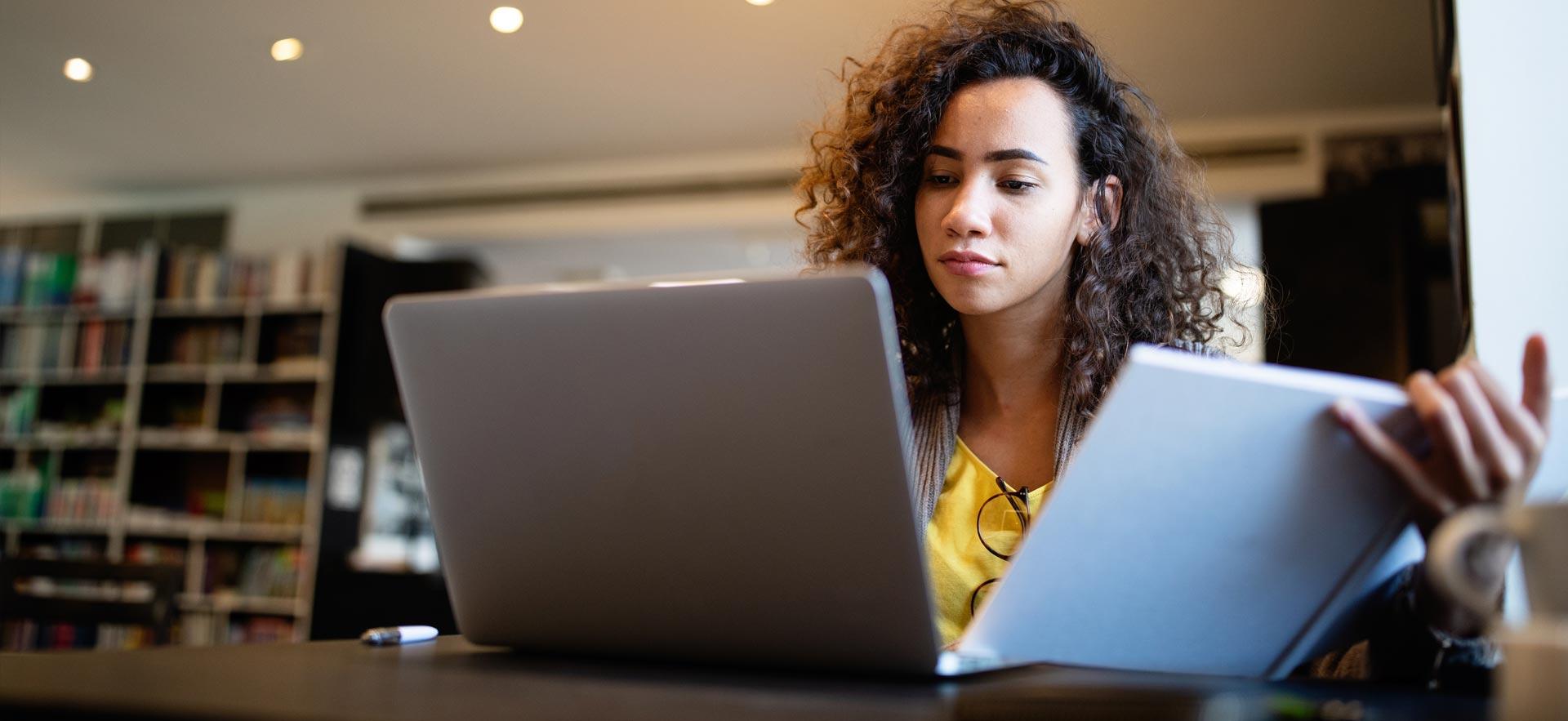 Young woman reading information on a computer and book.