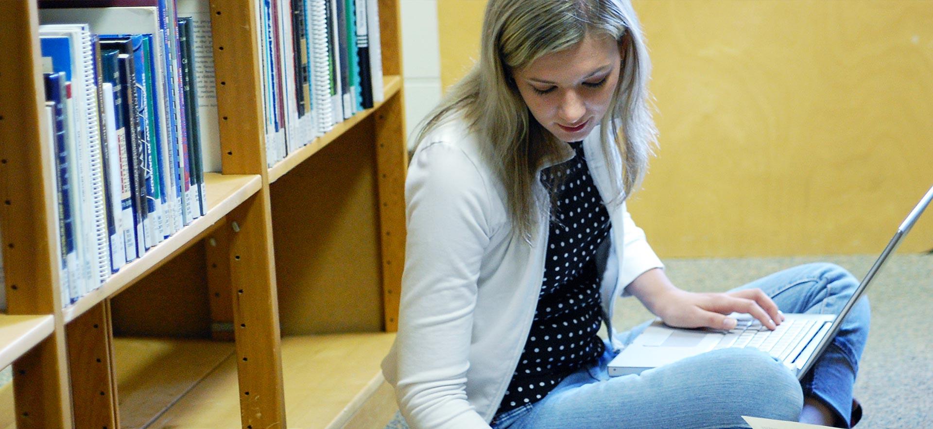 Young woman sitting down with her laptop in the Sault College library.