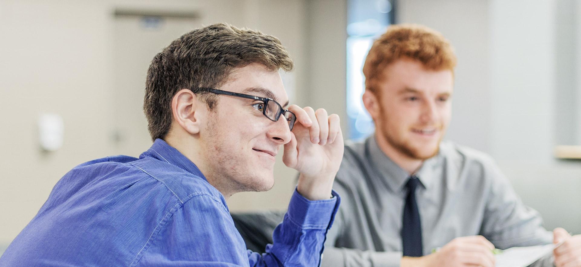 Male student smiling holding his glasses.