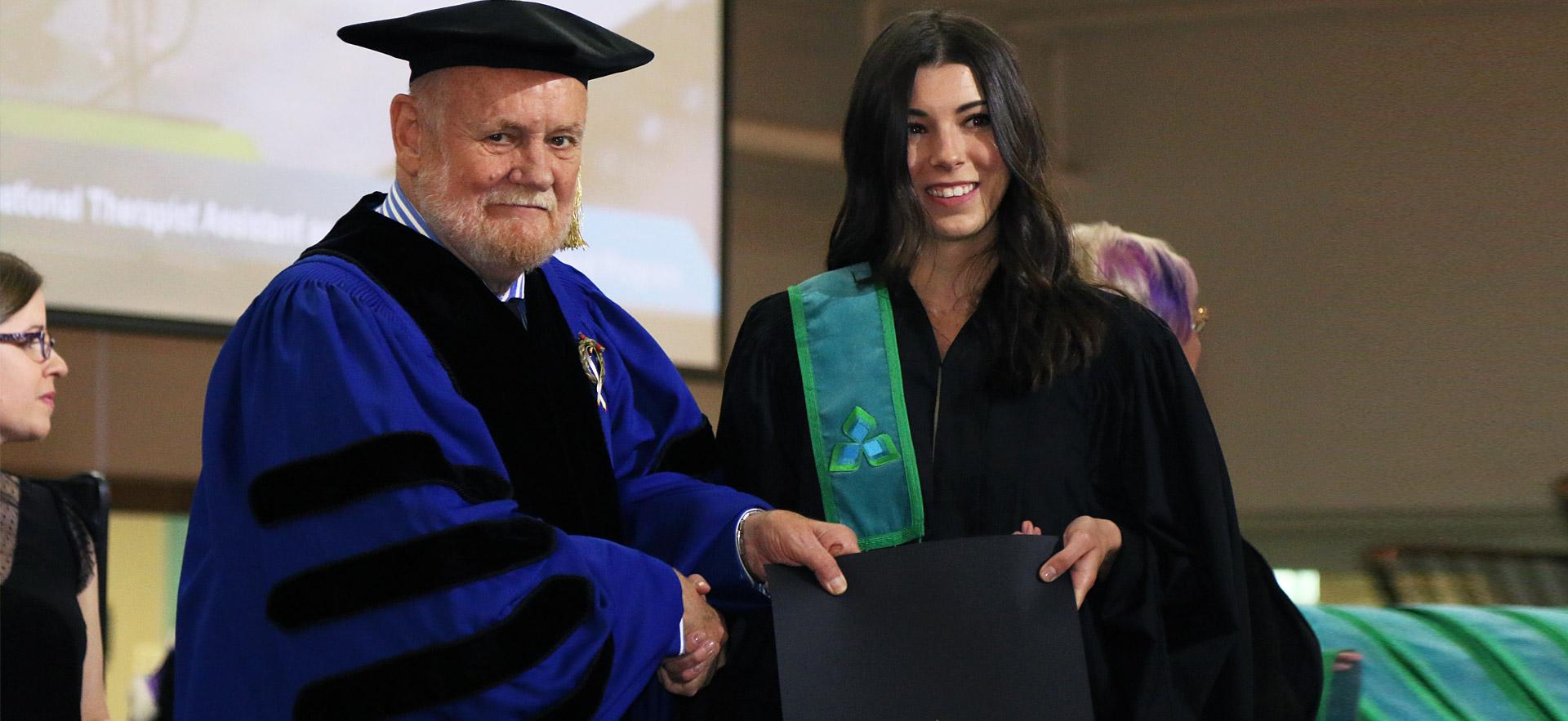 Female graduate receives her diploma from Ron Common.