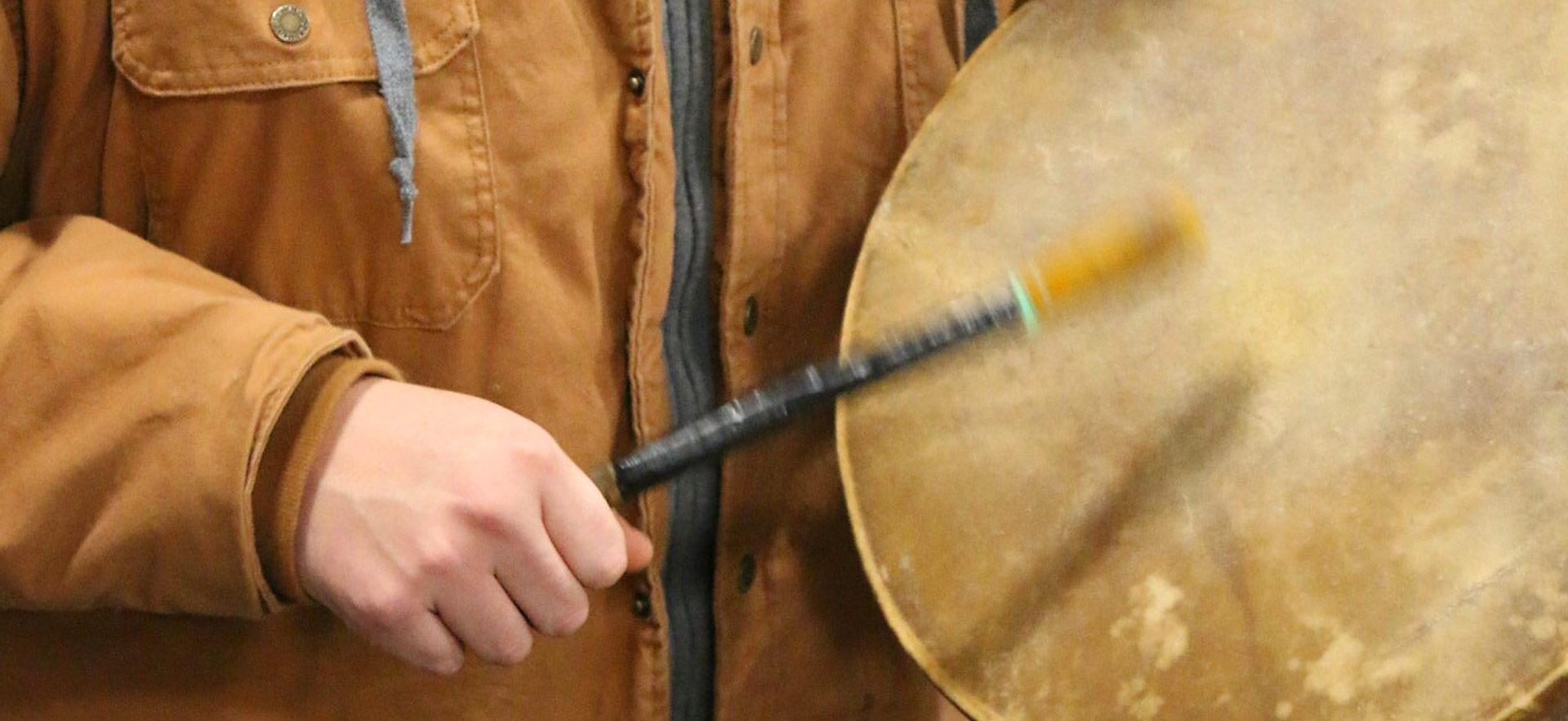 indigenous persons hand drumming with drum and drum stick