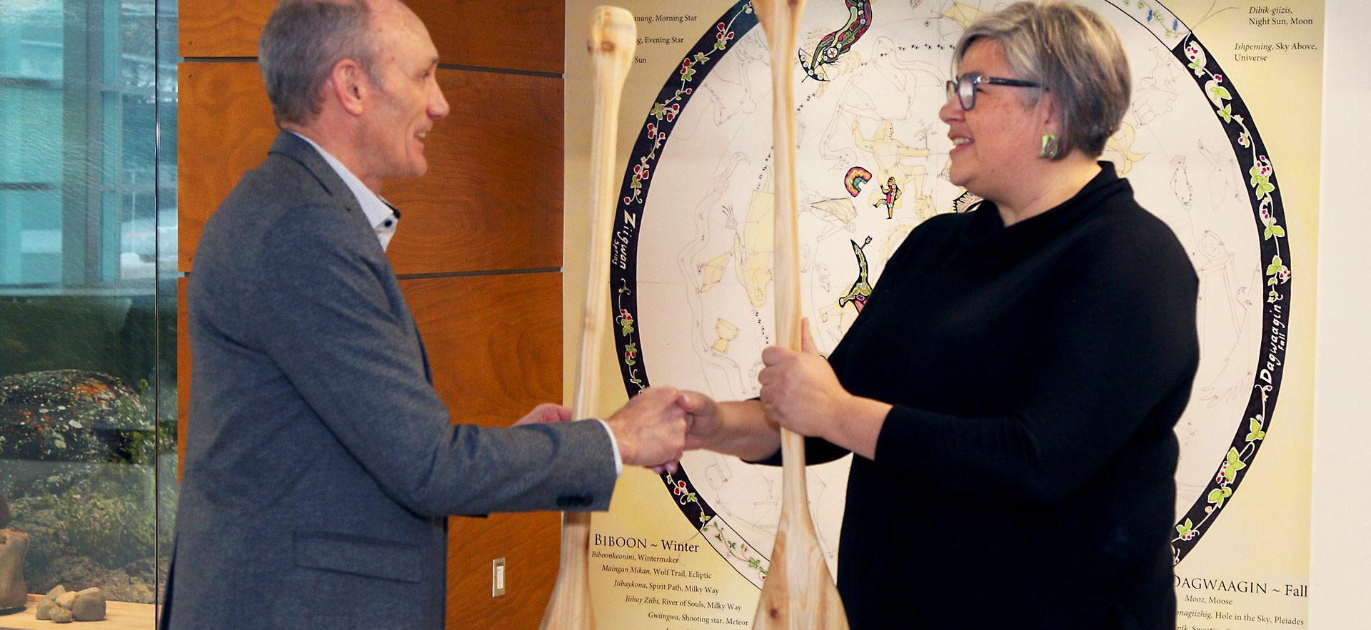 faculty exchanging canoe paddles with handshake