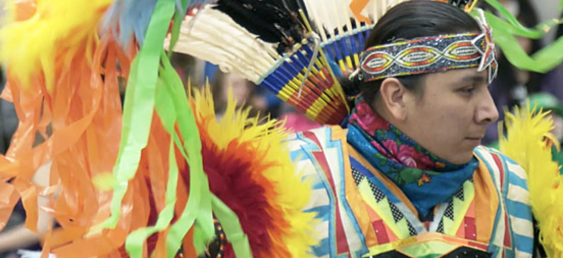 Wearing a colourful costume, an indigenous male dances at a pow wow.