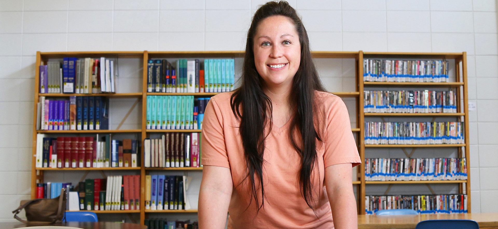 student standing and smiling in front of bookshelf