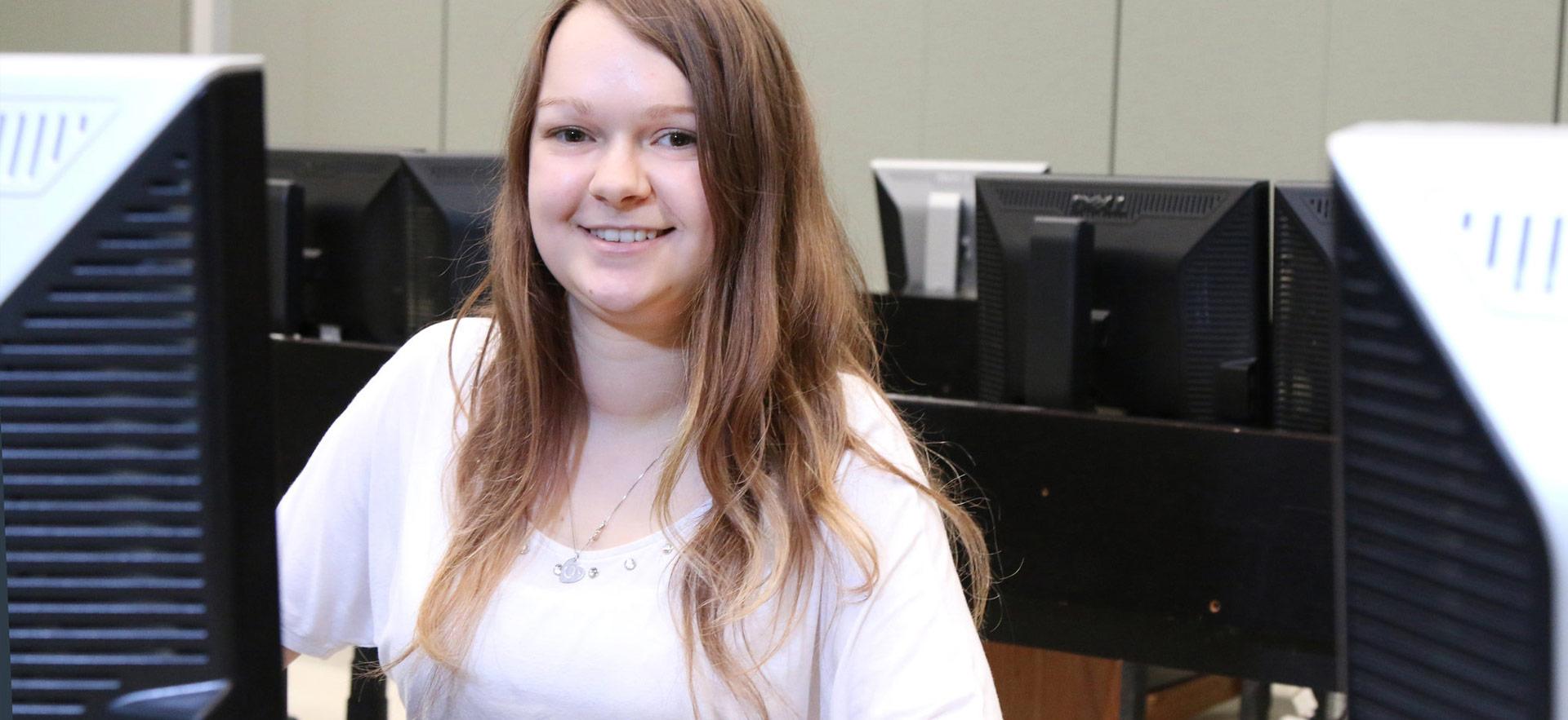 student smiling and siting at workstation computer