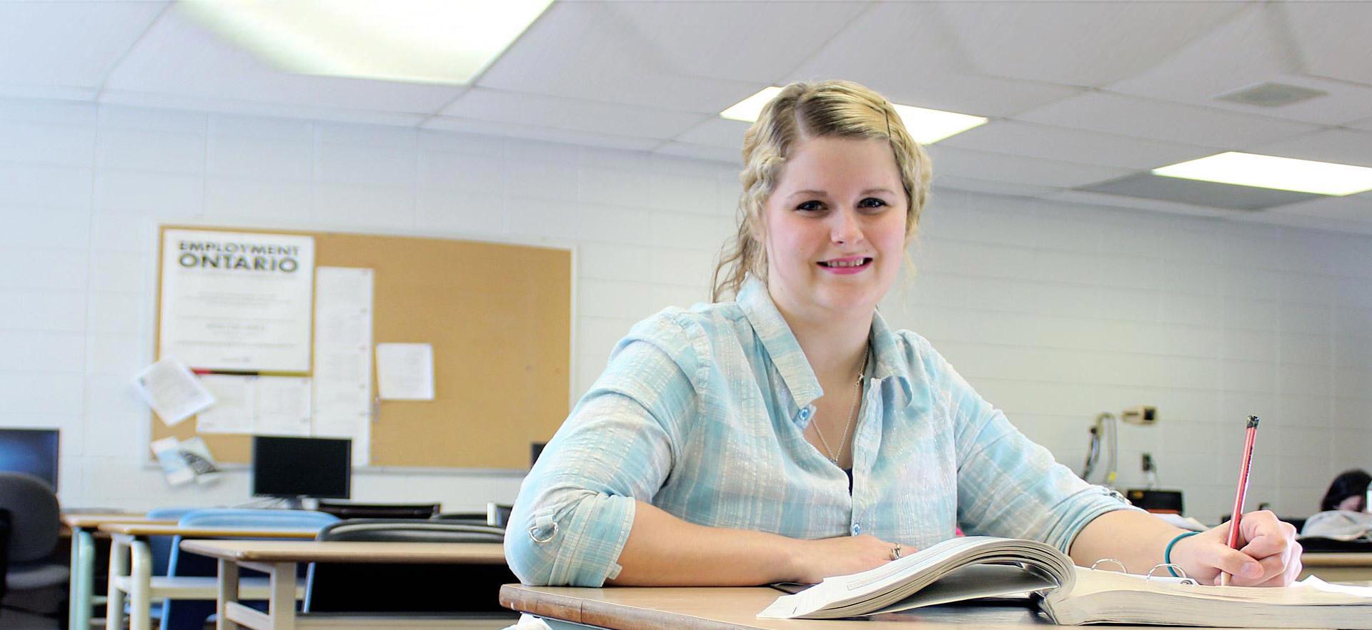 One female Academic Upgrading student smiles while sitting at her desk in class.