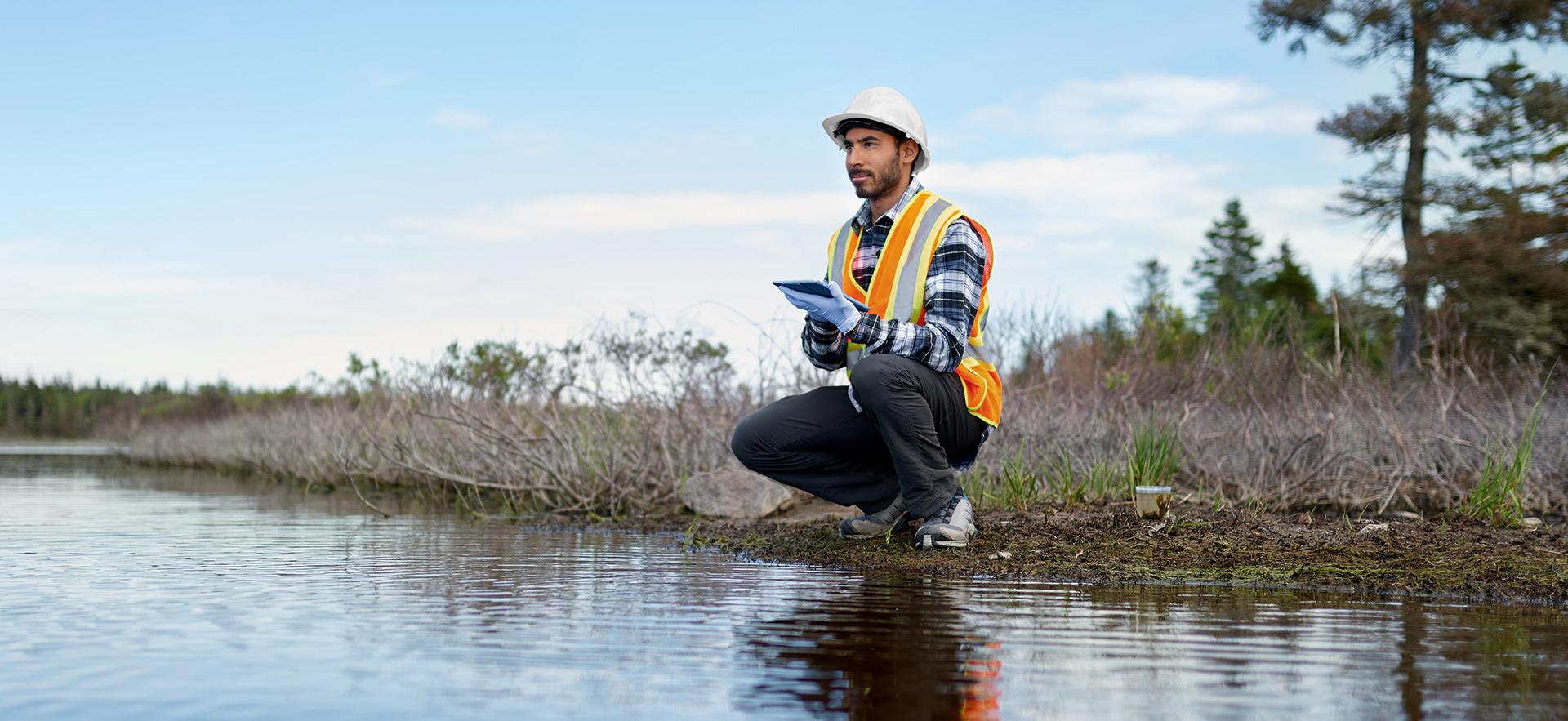 Person in orange vest and hard hat at shoreline of lake