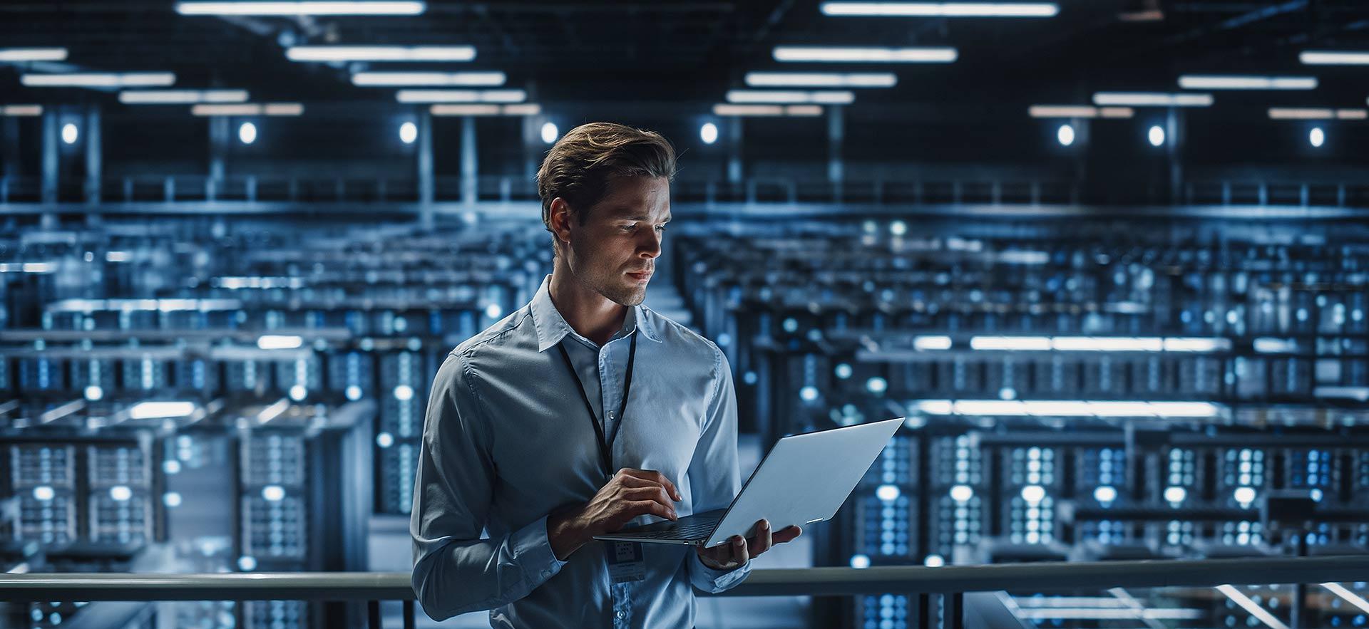 Man holding laptop with servers in background