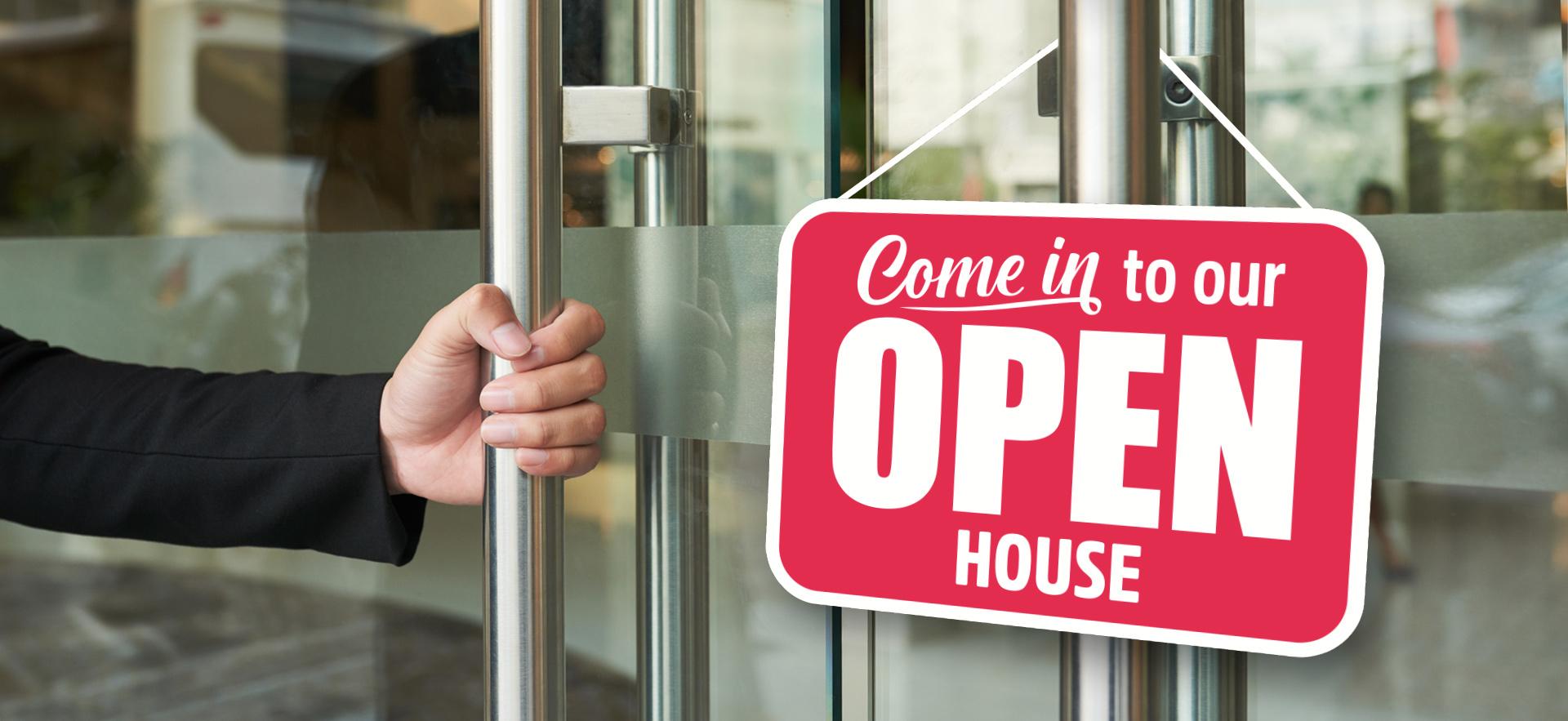 Glass doors with hand on one handle and sign hanging that says Come in to our OPEN HOUSE