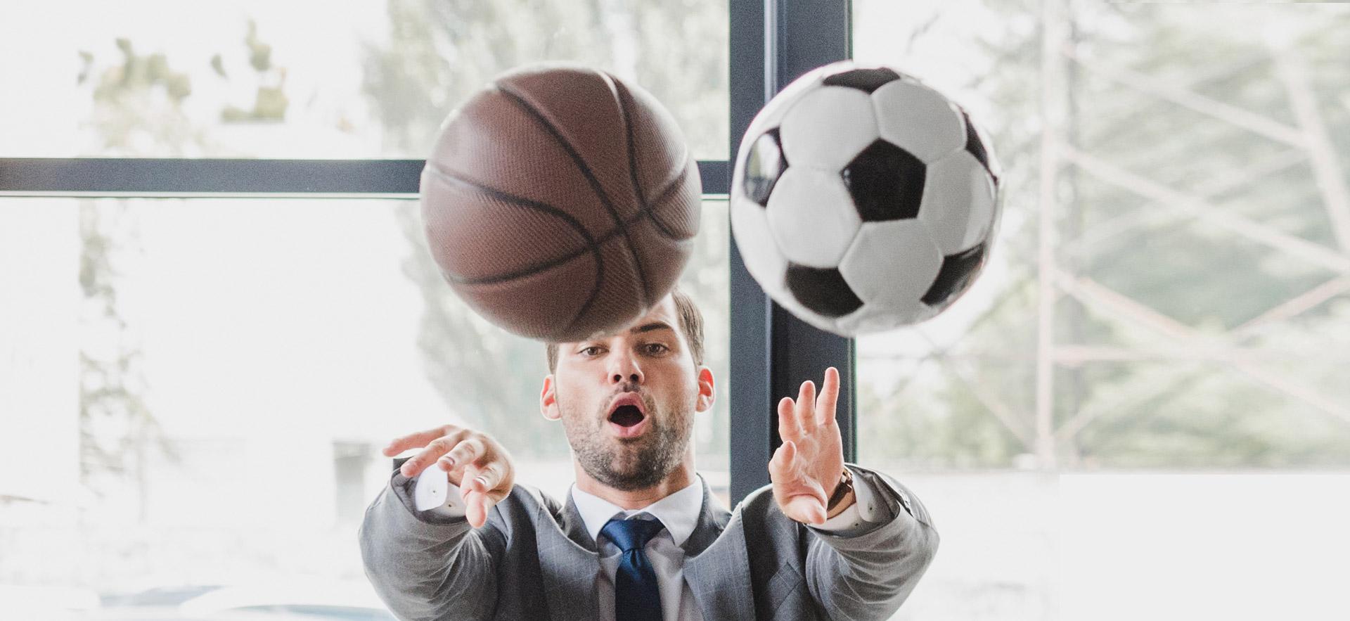 Man sitting at desk in a suit throwing a basketball and soccer ball