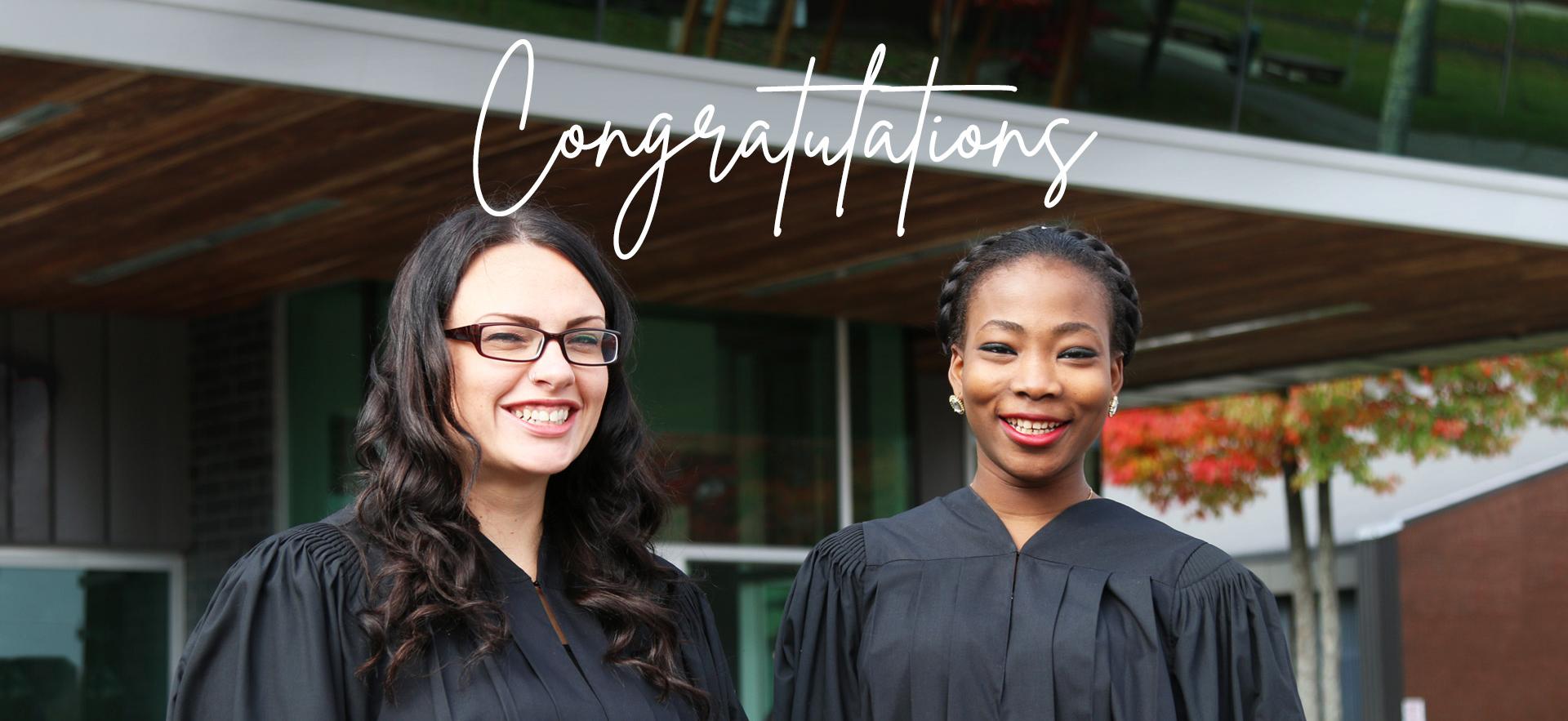 Two students wearing robes for convocation ceremony with congratulations written above in white script font