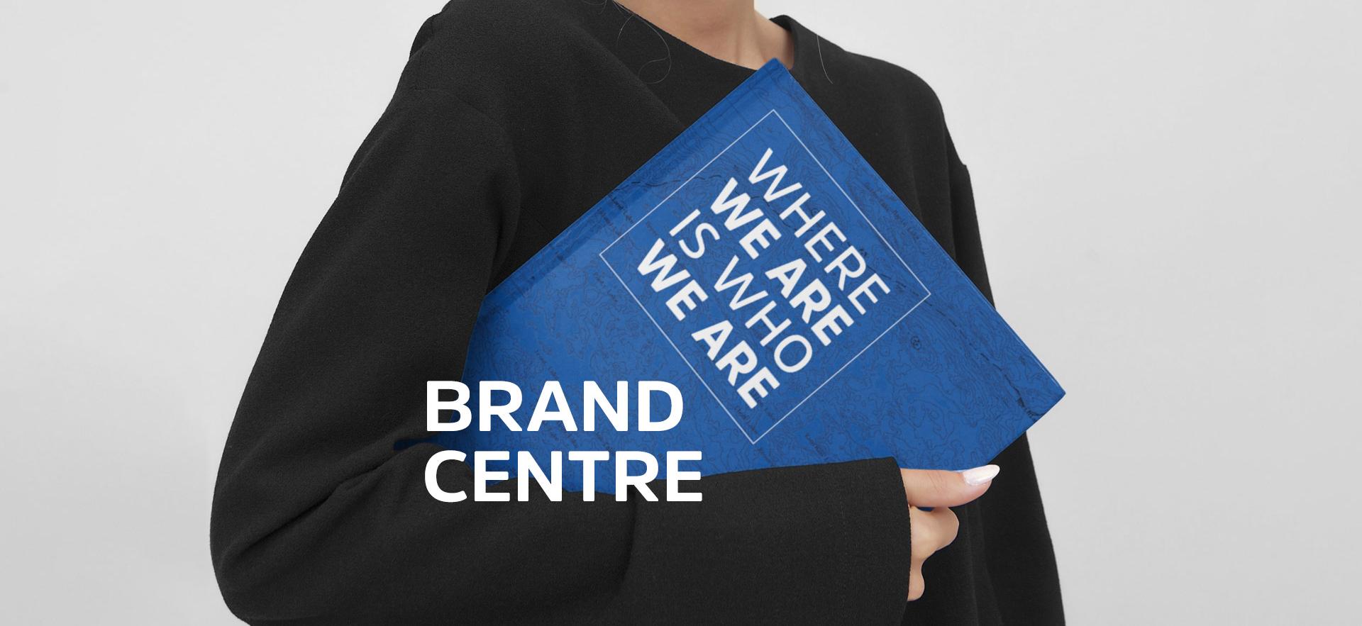 woman's chin to bottom of torso at angle with arm bent holding a Viewbook with Brand Centre text overlayed
