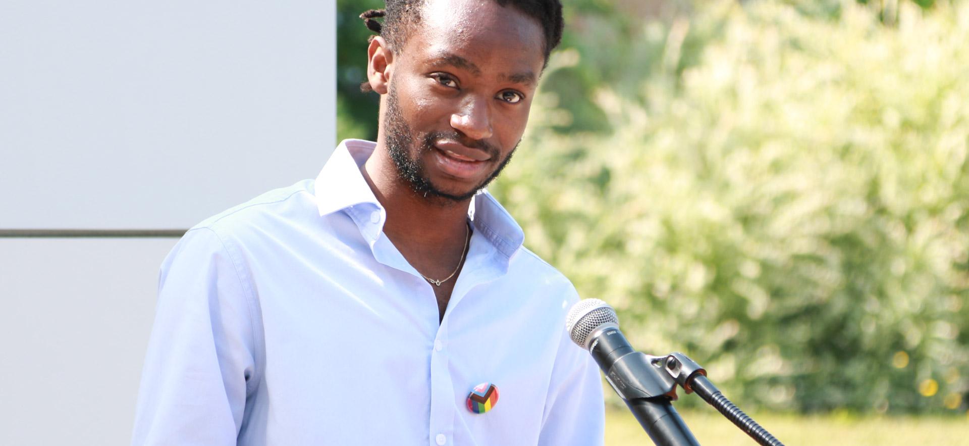 male with blue shirt speaking at a podium 