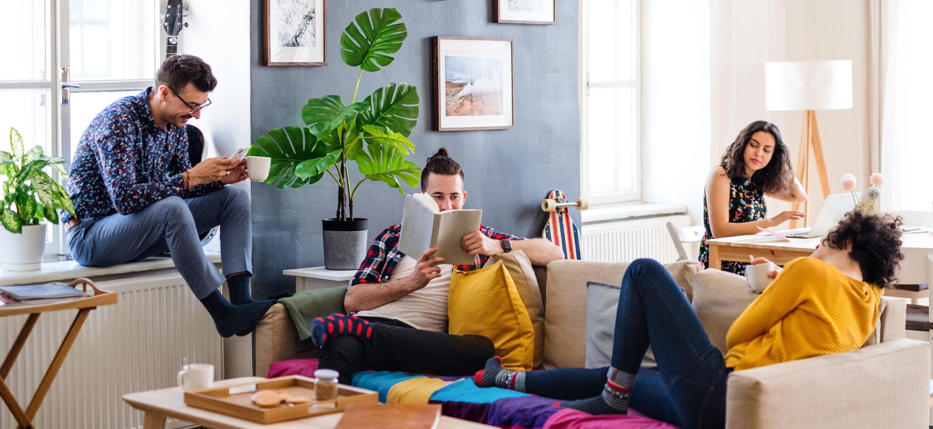 four students casually sitting in the living room and kitchen table chatting and looking at books