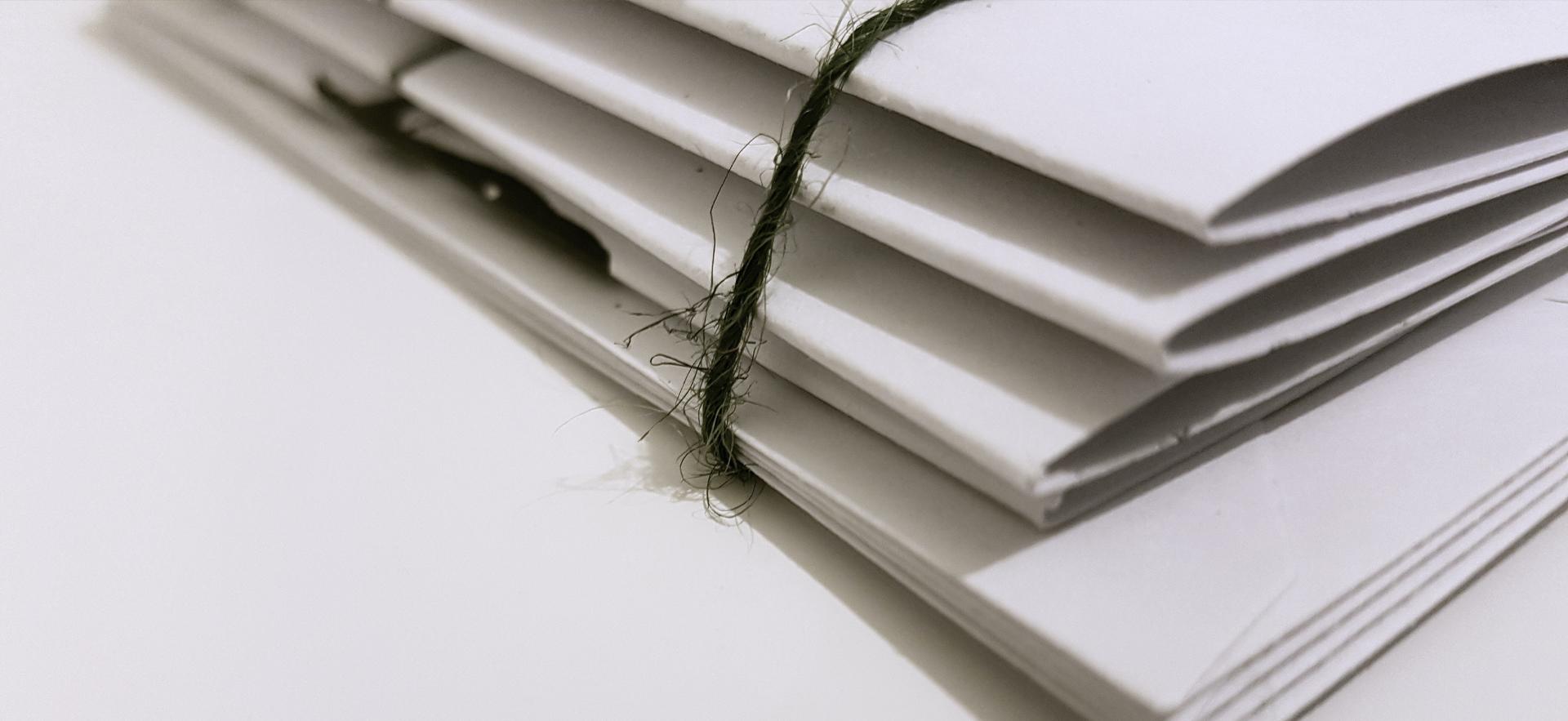 cut off image of white folders and enveloped piled with a black string wrapped around them