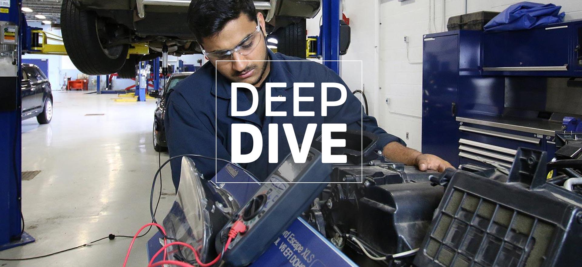 student in uniform in the Motive Power Centre looking down at car parts with lifted car in background