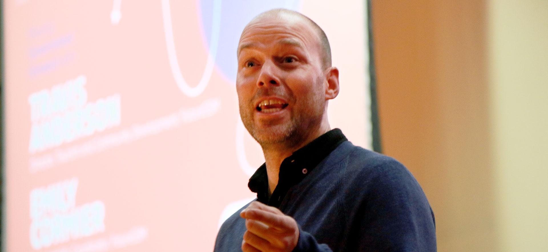 Man speaking to audience with hand out