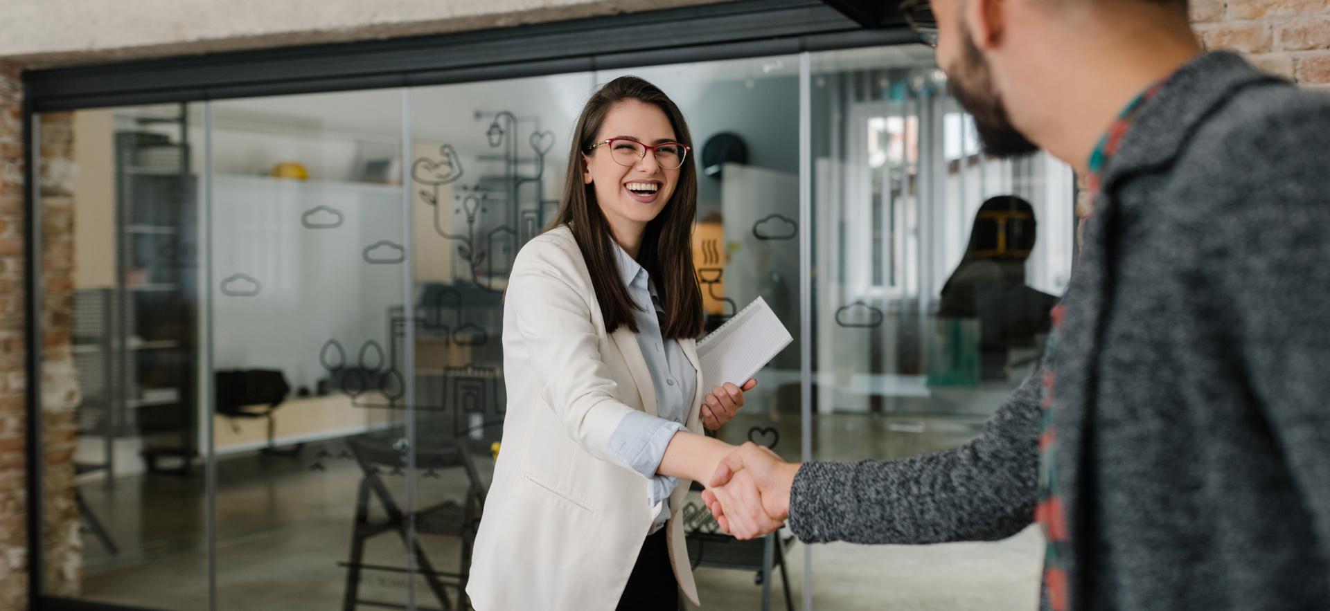 woman smiling shaking hands with man in a office with a large window wall