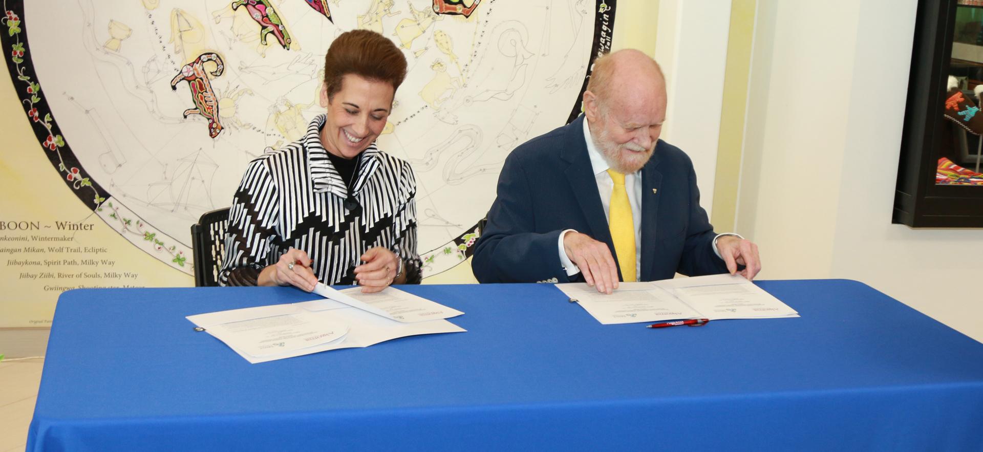 woman signing document with a man sitting beside her at a table with a blue tablecloth