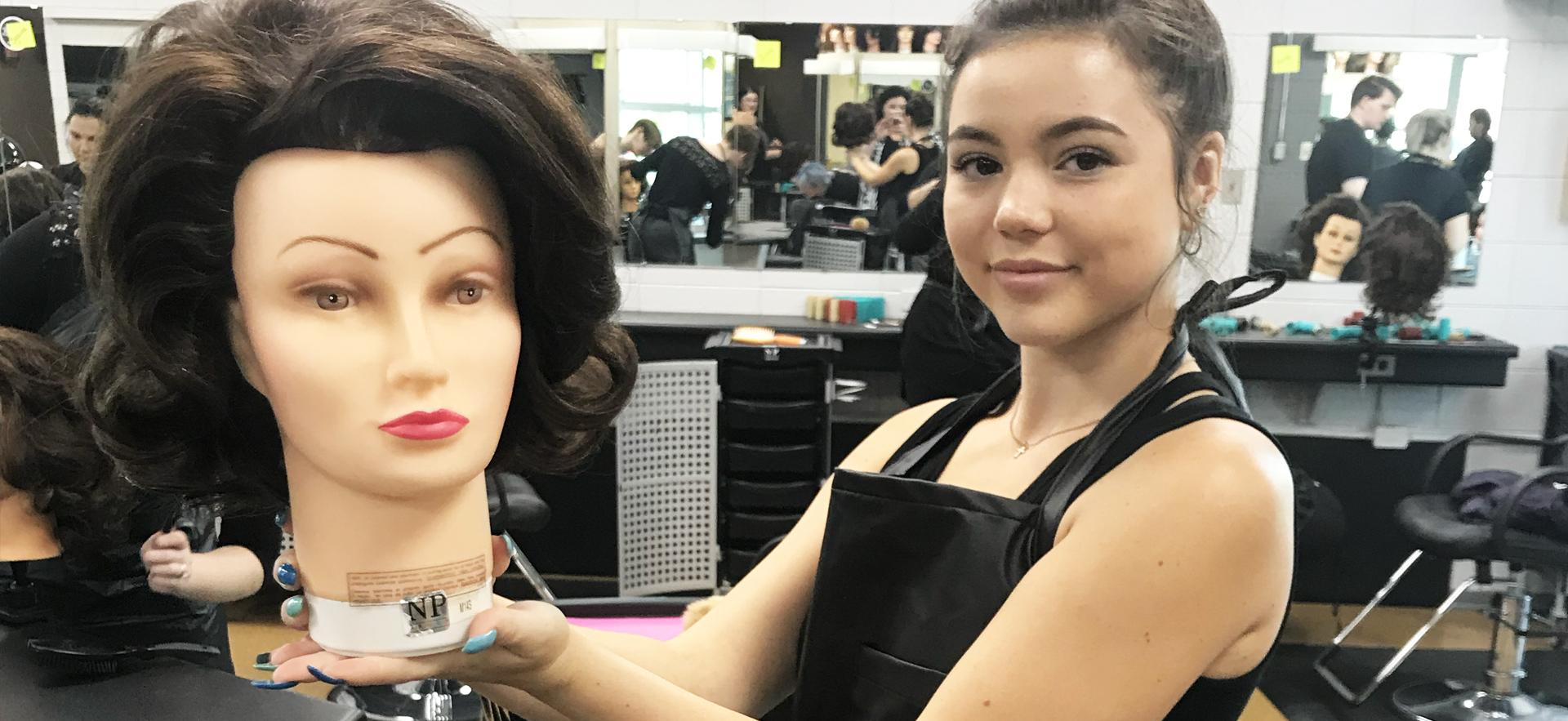 student showing finished hairstyle on a mannequin