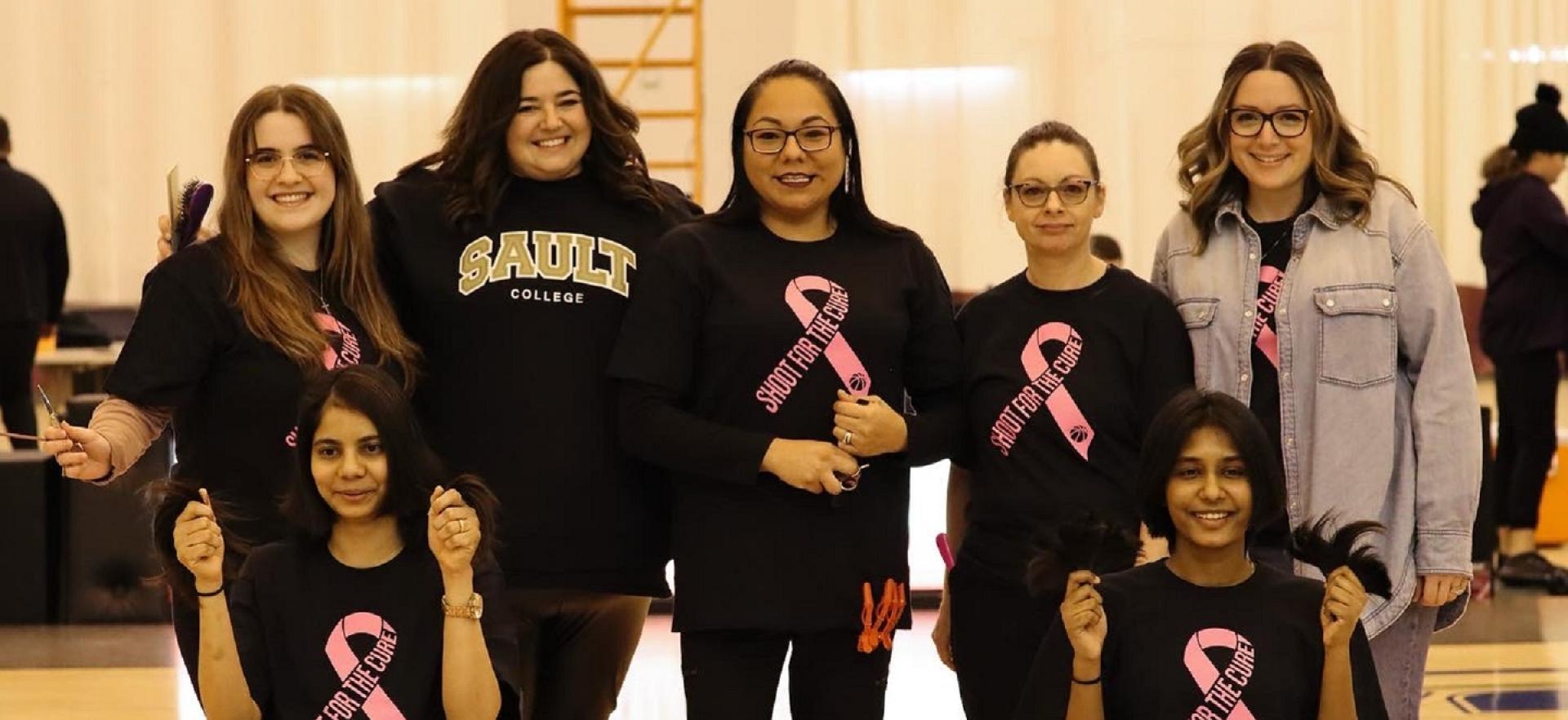 Hairstyling staff and students pose with two women whose hair they cut for cancer fundraiser