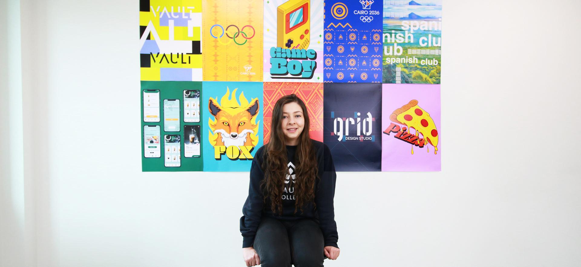 Graphic design student on a chair sitting in front of posters of their work