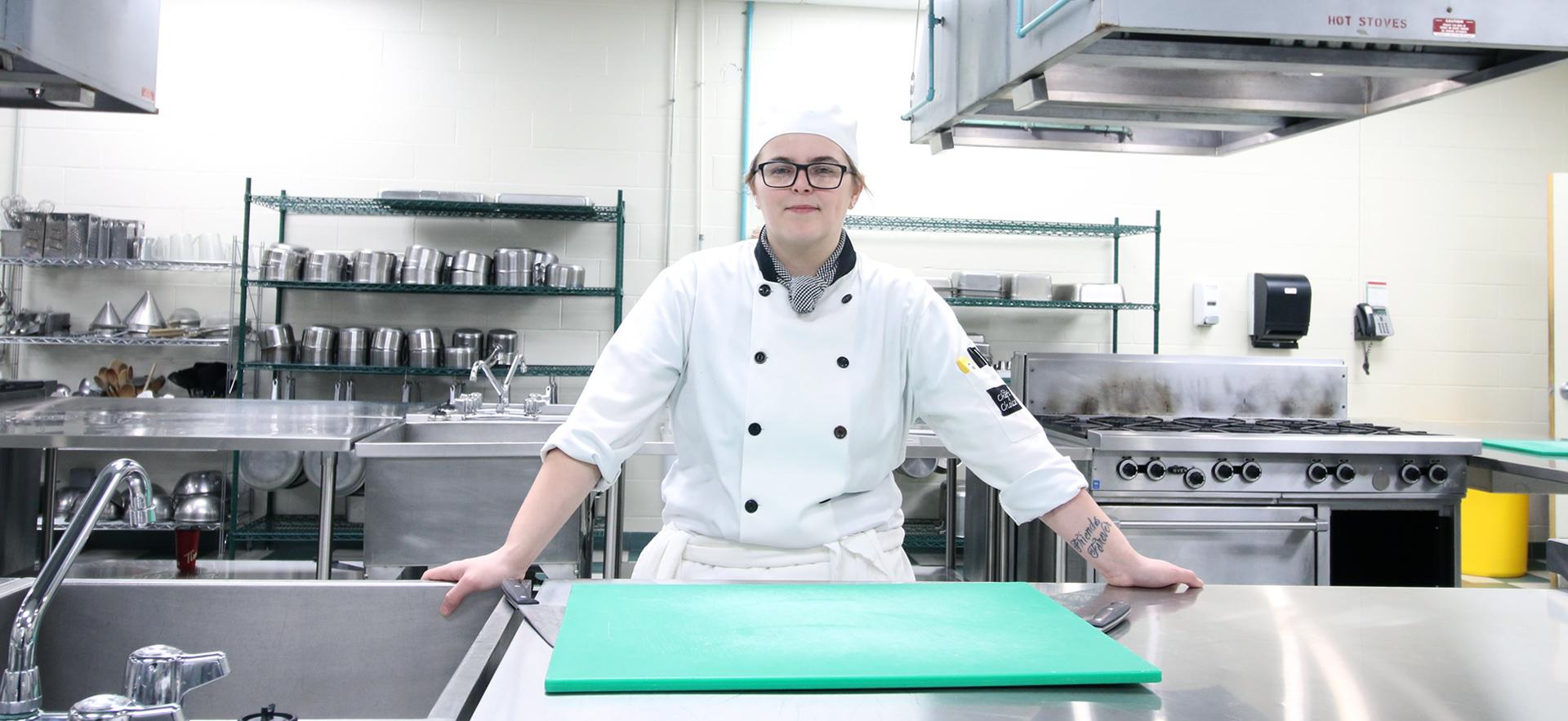 Culinary student in uniform posed at counter in culinary lab looking at camera