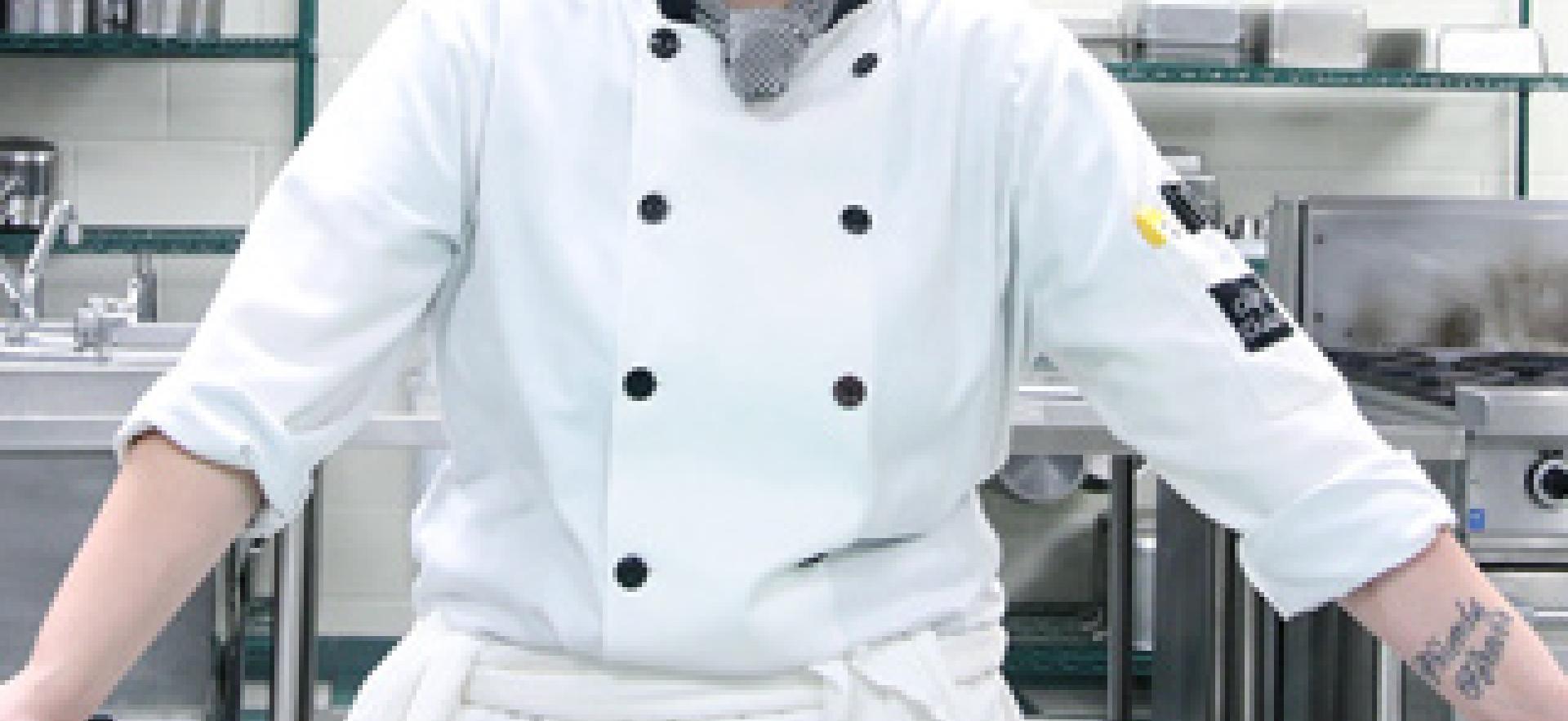 Culinary student in uniform posed at counter in culinary lab looking at camera