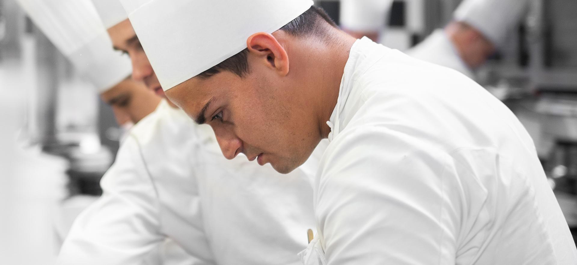 Josh Adamo graduate shown in chef uniform in kitchen