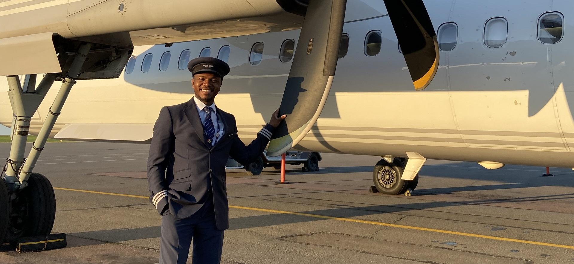 George smiling at camera beside plane holding propeller