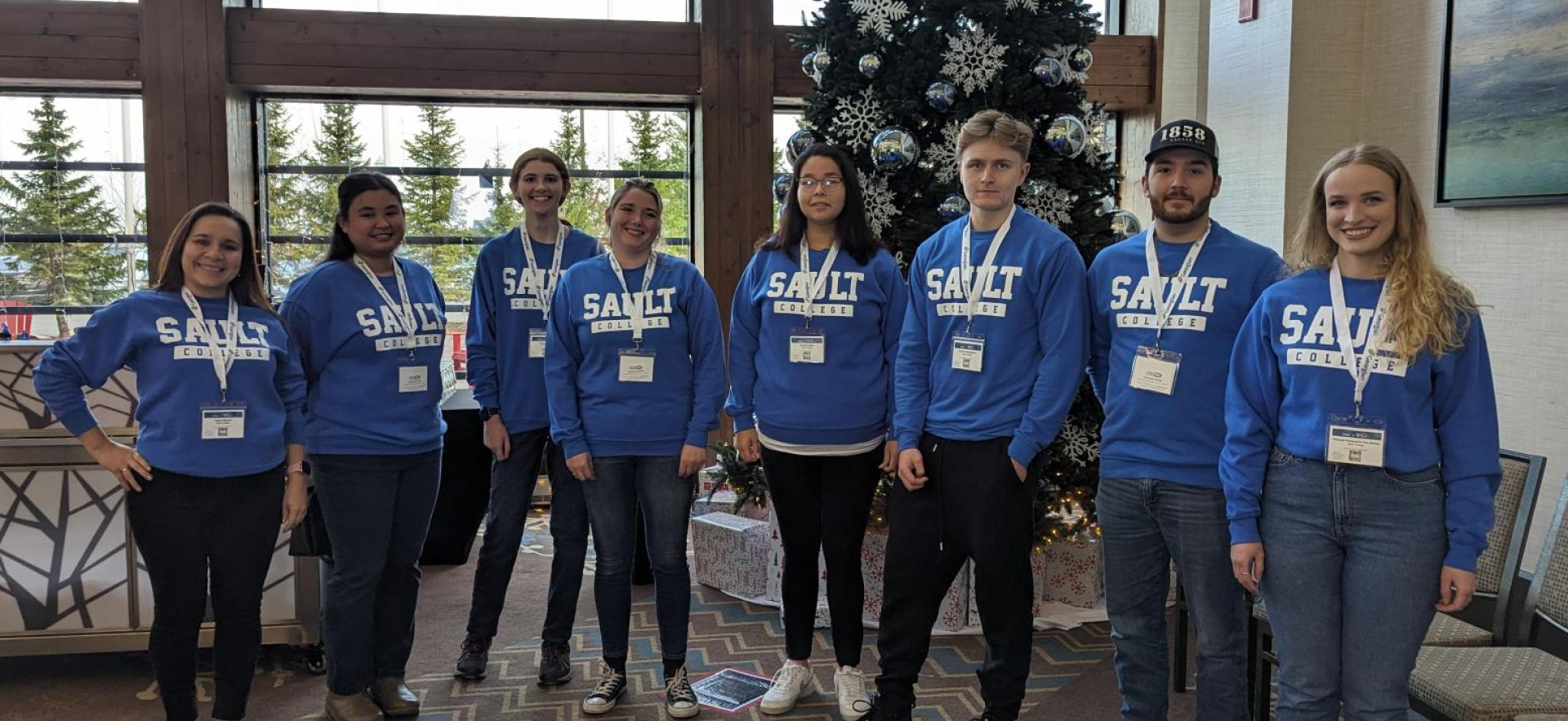 eight students standing in a line beside each other. Each are wearing the same blue sweater with Sault College written on the front in white letters. 