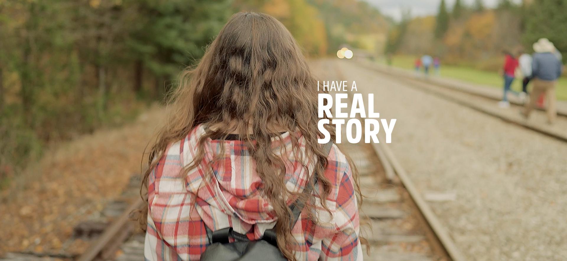 Graduate walking away on train tracks with her back facing the camera