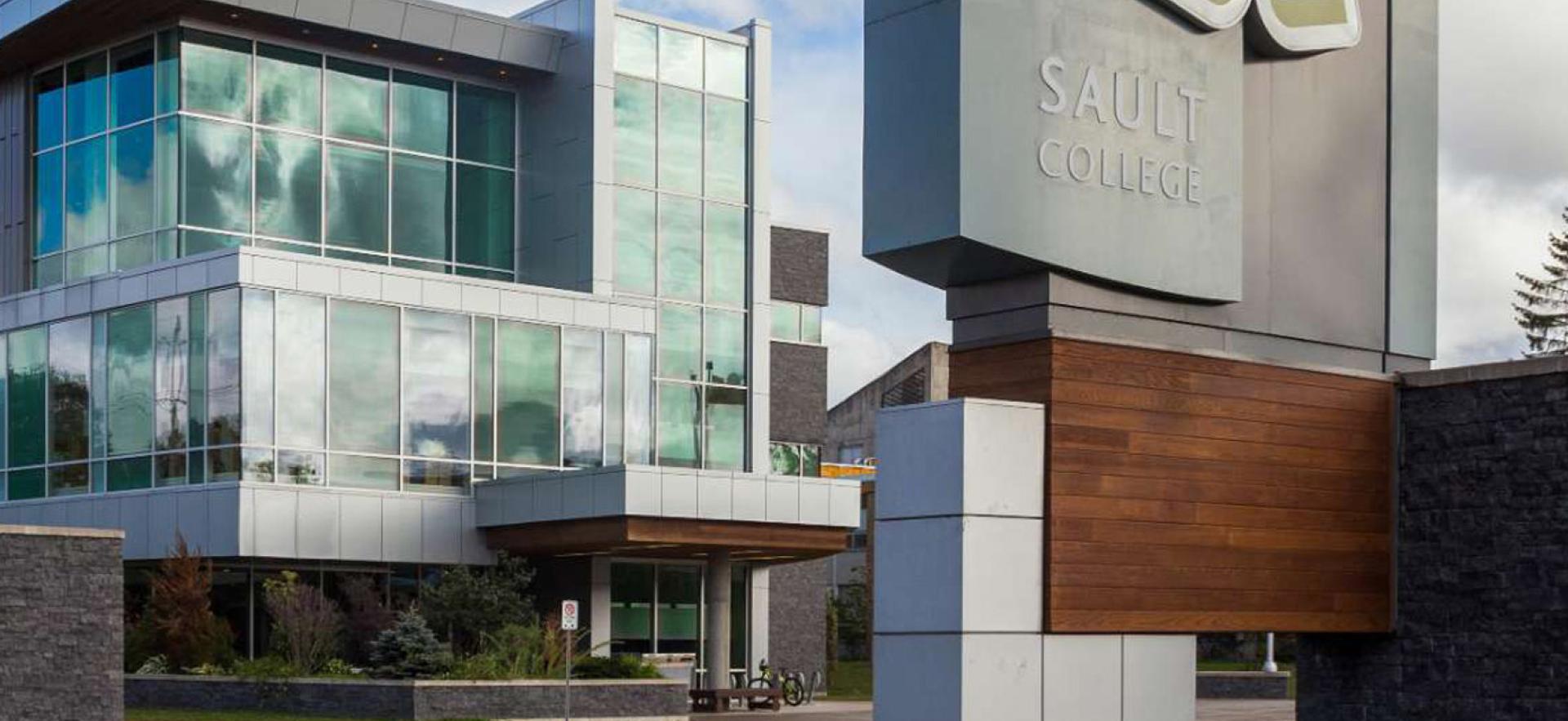 Campus at main entrance showing sign with building behind with a partly cloudy sky