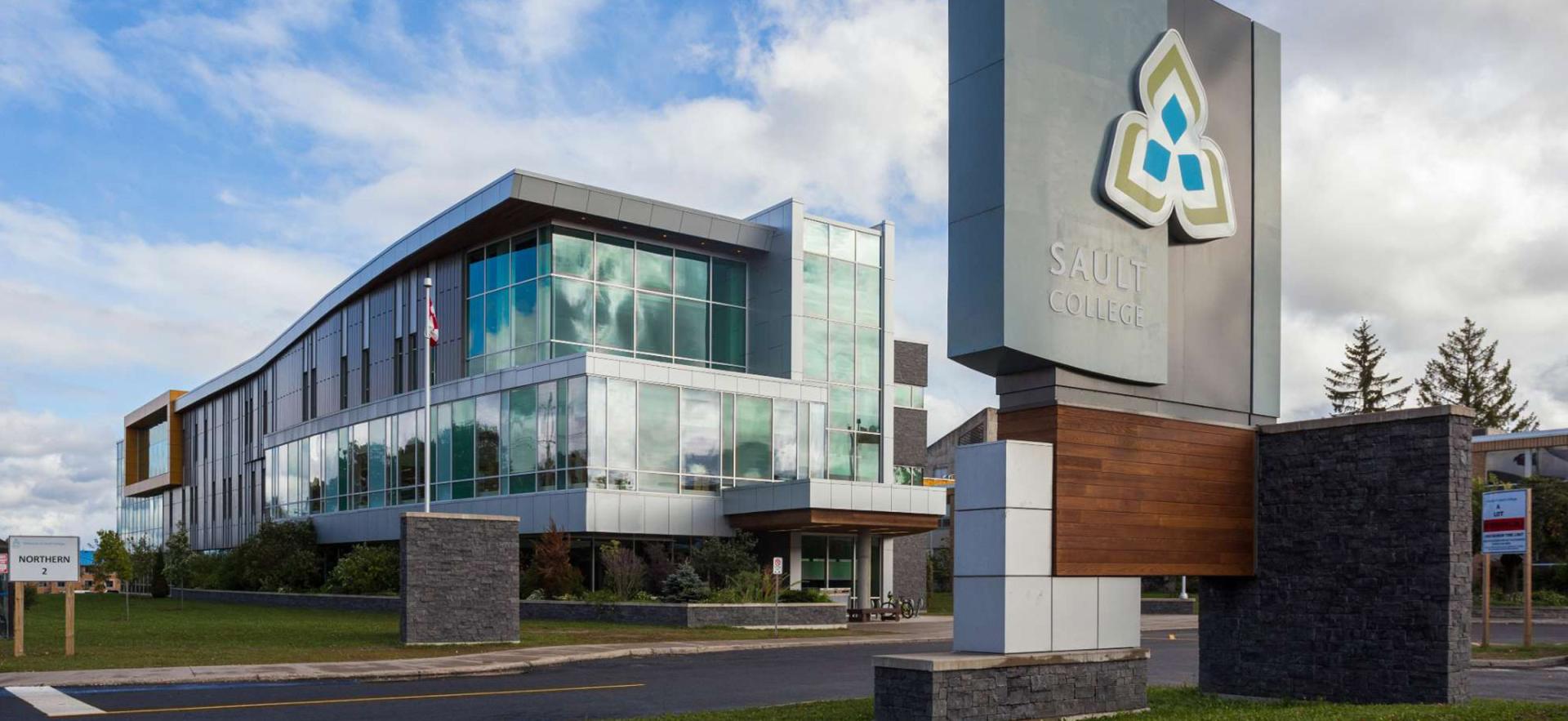 Campus at main entrance showing sign with building behind with a partly cloudy sky